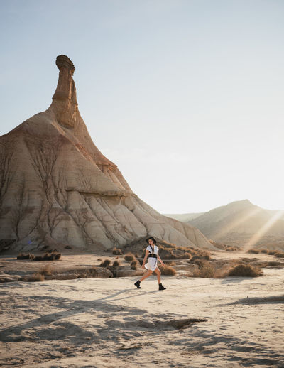 Full body young female tourist strolling on sandy terrain near mountain ridge in natural park of bardenas reales in navarre province of spain