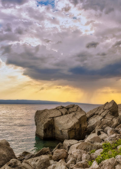 Rocks by sea against sky during sunset