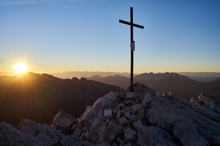 Cross on rock against sky during sunset