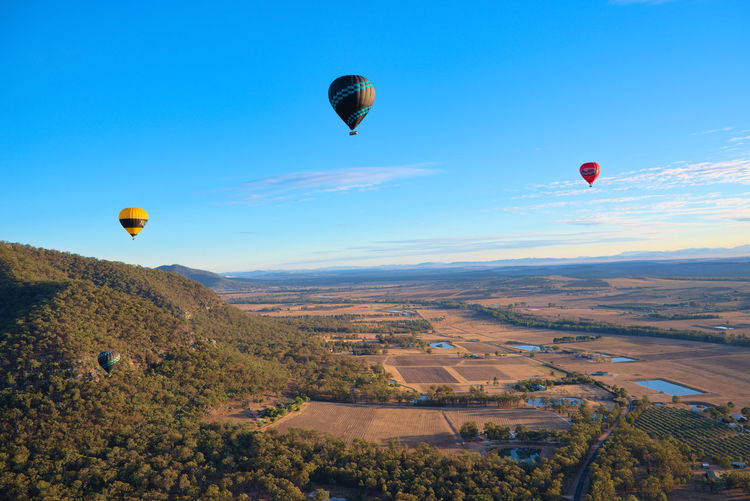 Hot air balloons flying over landscape against blue sky