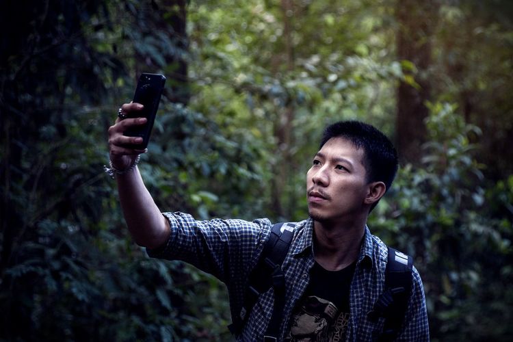 Portrait of man photographing through smart phone in forest