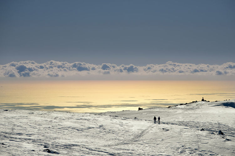 People on snow covered landscape against sky during sunset