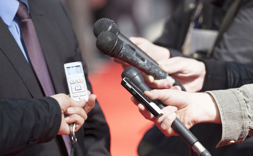 Midsection of reporters holding microphone by businessman