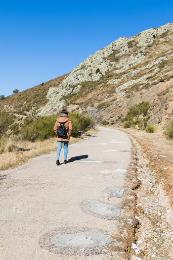 Rear view of woman walking on road against mountain and clear sky