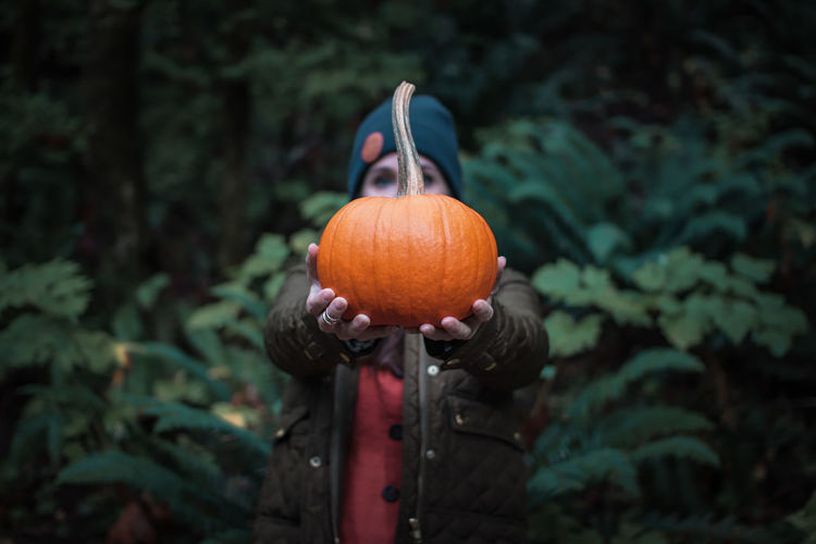 Portrait of mid adult woman holding pumpkin in forest during autumn