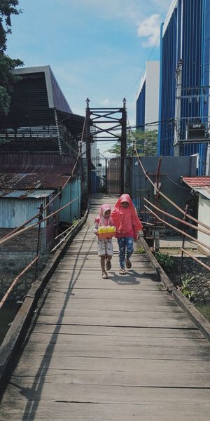 Full length of girls walking on footbridge amidst building