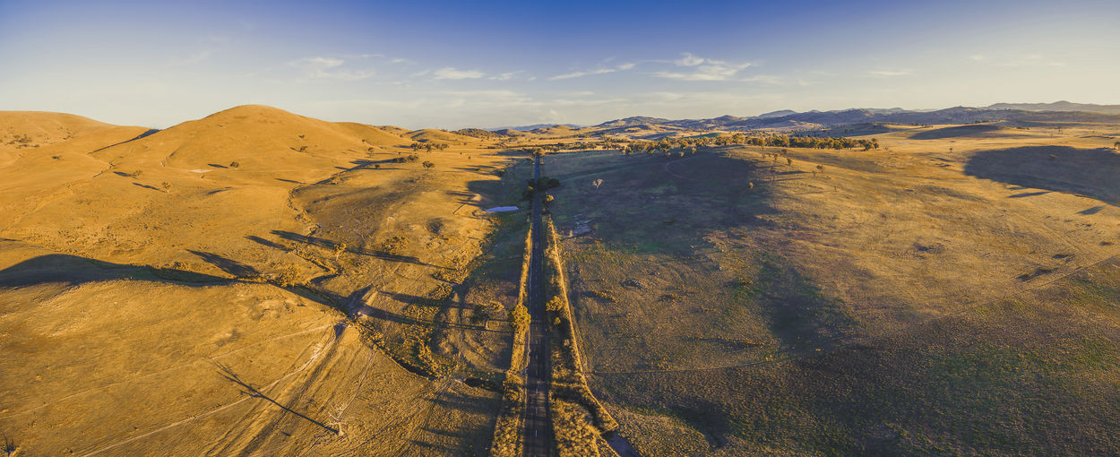 Aerial panorama of straight rural road passing through countryside at sunset