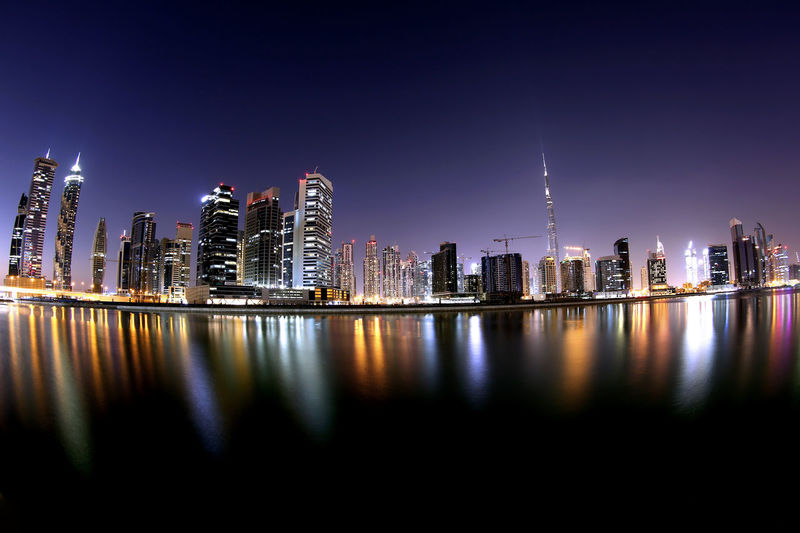 Low angle view of illuminated city reflecting in river against clear sky