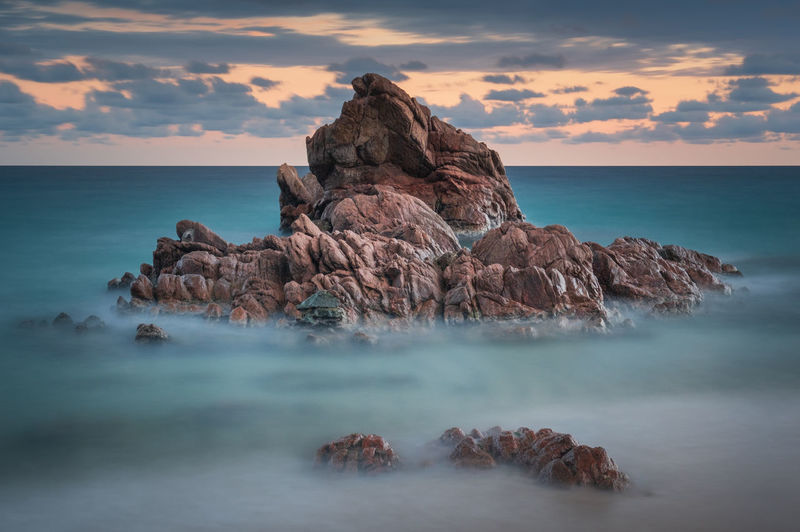 Rocks in sea against sky during sunset