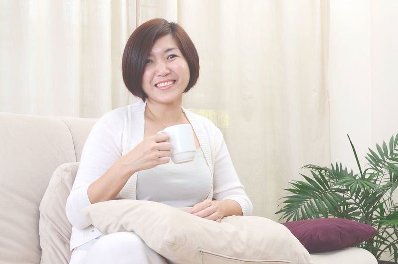 Portrait of smiling woman having coffee while sitting on sofa at home