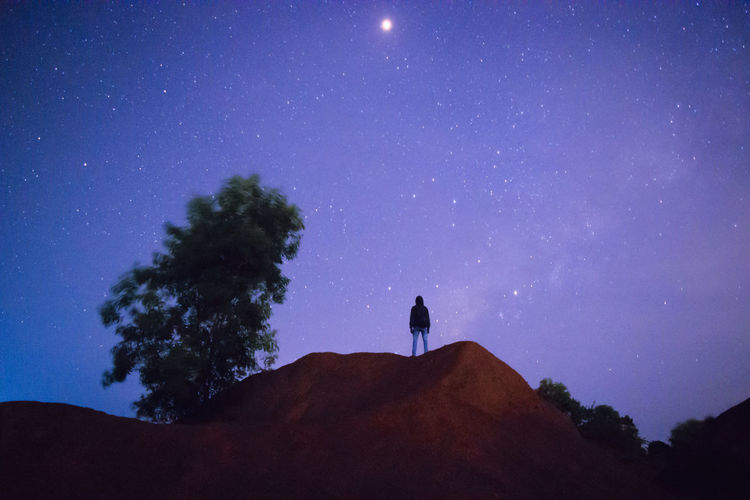 Low angle view of silhouette mid adult man standing on mountain against star field at night