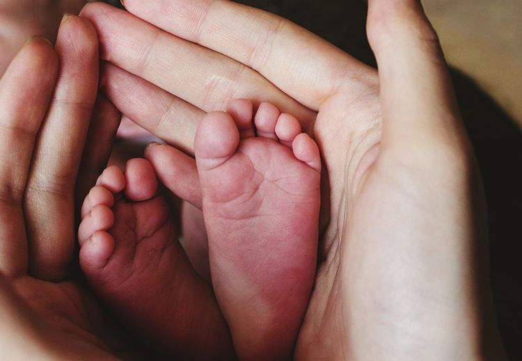 Close-up of mother hands holding baby feet at home