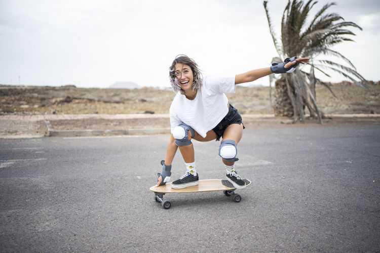 Happy young woman practicing skateboarding on road