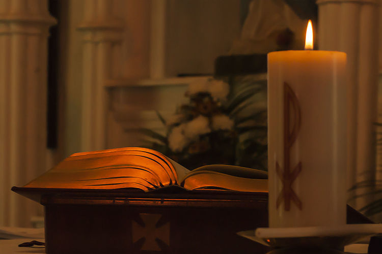 Close-up of lit candle and bible on altar