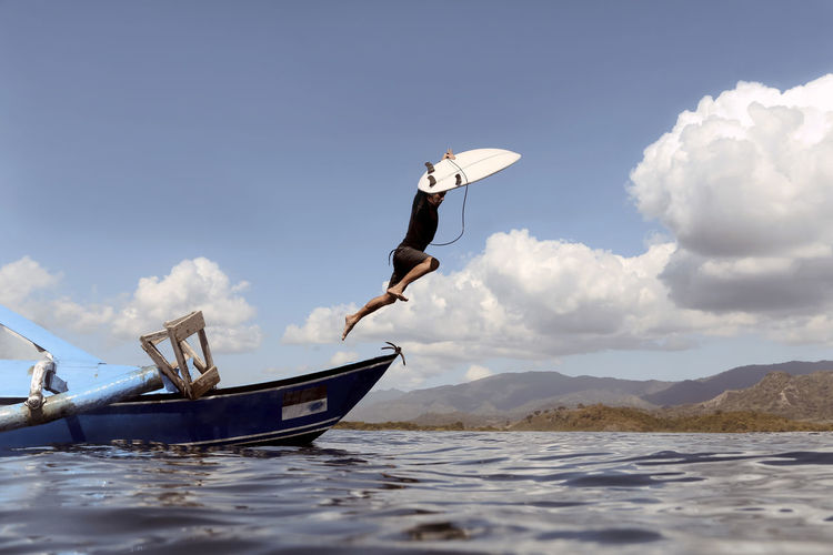 Side view of man jumping in sea against sky