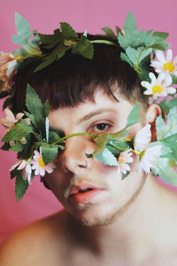 Close-up portrait of young man wearing flower against pink background