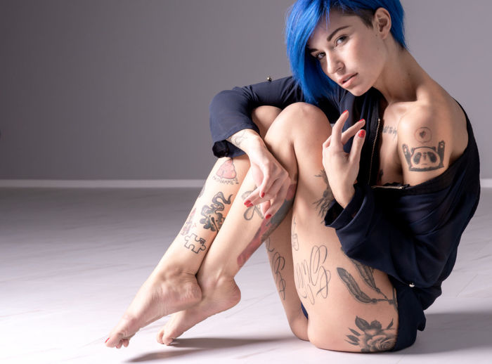 Full length portrait of seductive tattooed woman sitting on floor at home