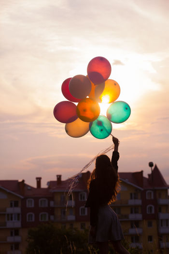 Rear view of woman with balloons against sky during sunset