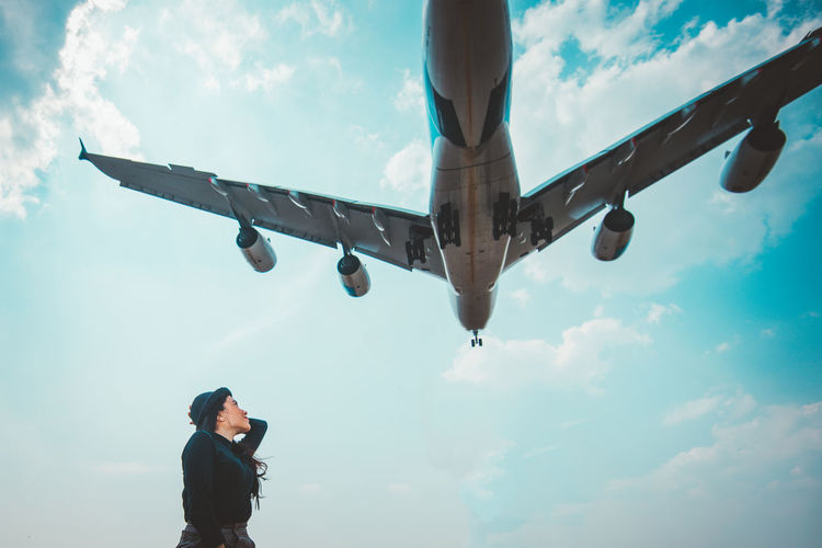 Woman looking at airplane flying against sky