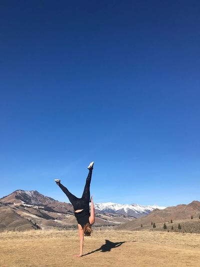 Full length of woman practicing handstand on field against clear blue sky