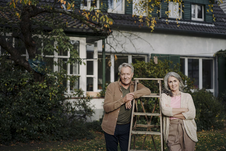 Portrait of senior couple with a ladder in garden of their home