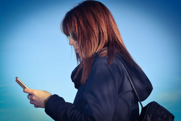 Side view of woman using phone against sky