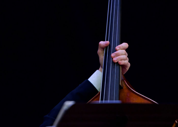 Cropped hand playing string instrument against black background