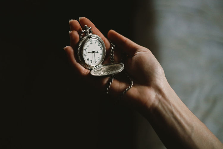 Close-up of hand holding pocket watch against black background