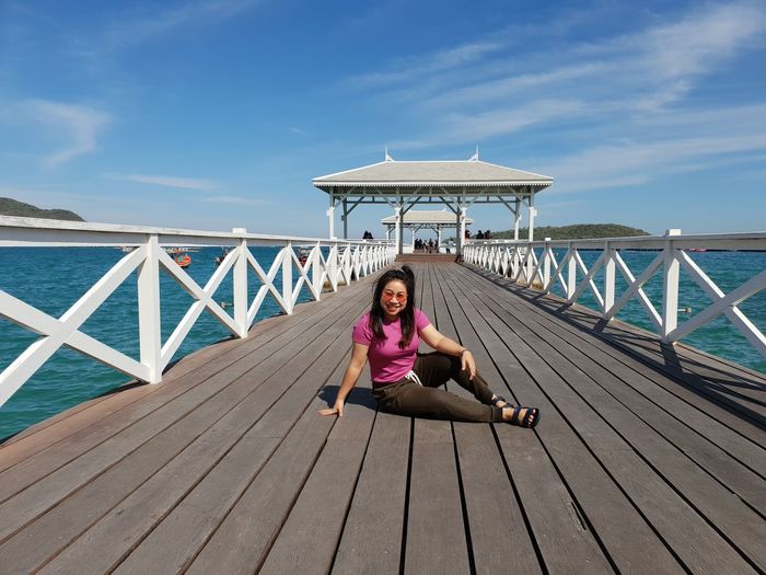 Full length of woman sitting on pier over sea against sky