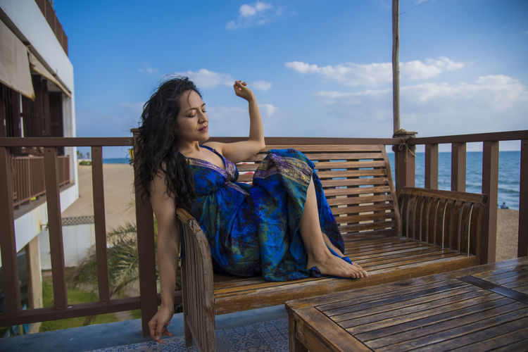 Young woman relaxing on bench in balcony against sea