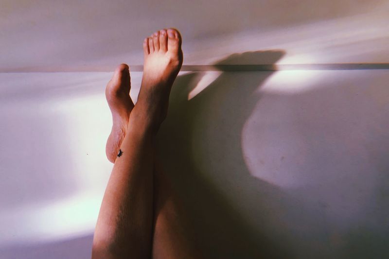 Low section of woman feet resting on wall at home