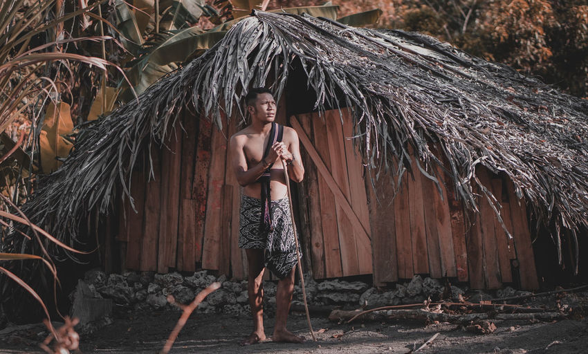 Full length of shirtless man standing against hut