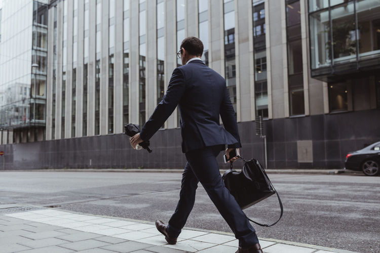 Full length of entrepreneur with bag walking on sidewalk in city