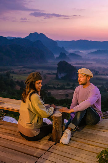 Side view of man sitting on mountain during sunset