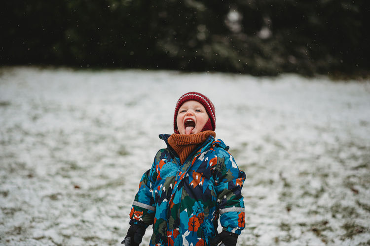 Adorable child sticking his tongue out tasting snowflakes in winter