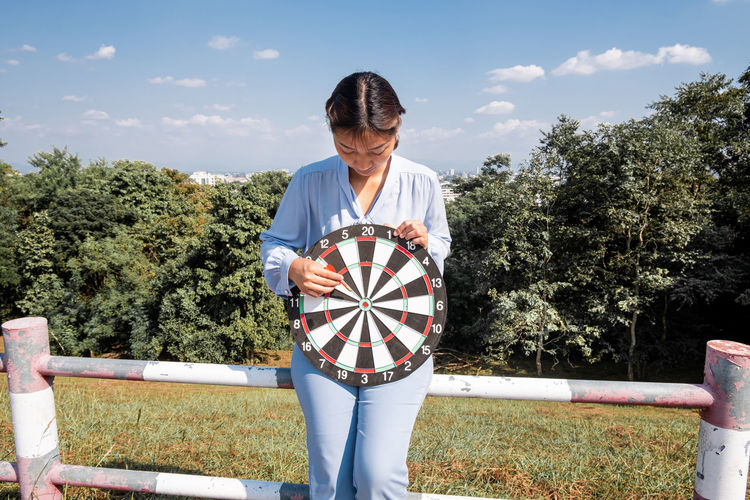 Young woman holding dart board against sky