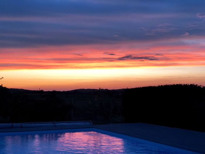 Silhouette trees by swimming pool against sky during sunset