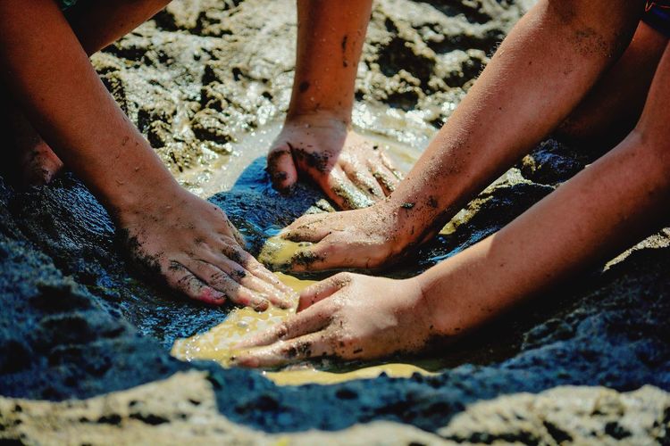 Cropped hands of children playing with wet sand at beach