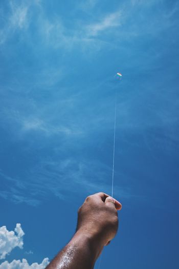 Cropped hand of man flying kite against blue sky
