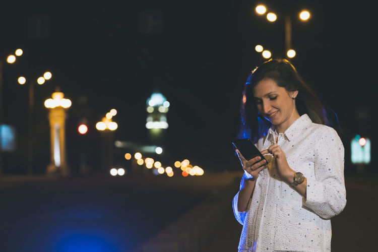 Attractive girl in white suit using smartphone in night, light reflection
