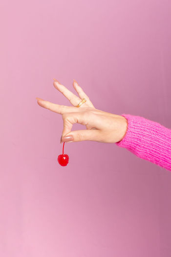 Cropped hand of woman holding red heart shape against pink background