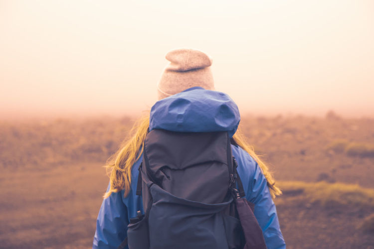 Rear view of woman with backpack standing on field during foggy weather