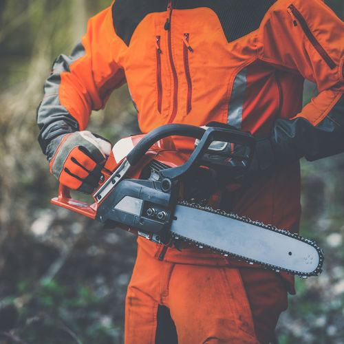 Hand holding a chainsaw. lumberjack at work gardener working outdoor in the forest. worker concept