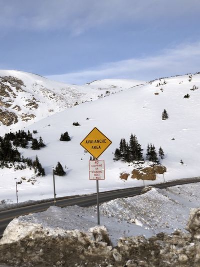 Road sign by snow covered mountain against sky