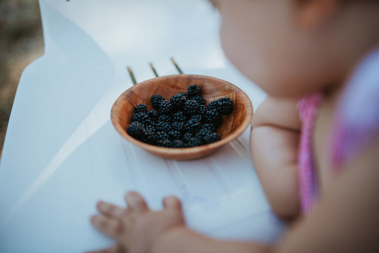 Close-up of baby girl by bowl with blackberries