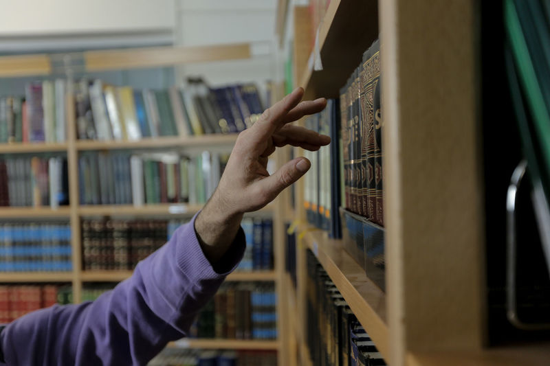 Cropped hand of man touching book in shelf