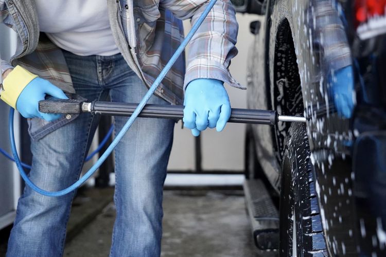 Midsection of man cleaning car with equipment in garage