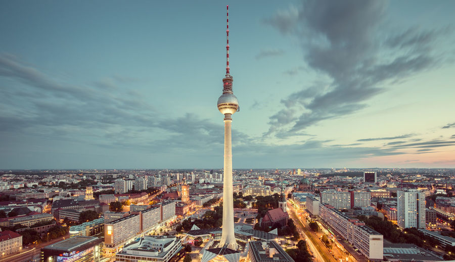 Television tower in illuminated city during sunset