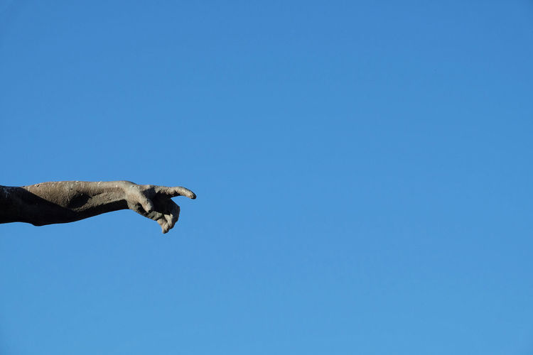Statue arm with pointing hand, blue sky as background