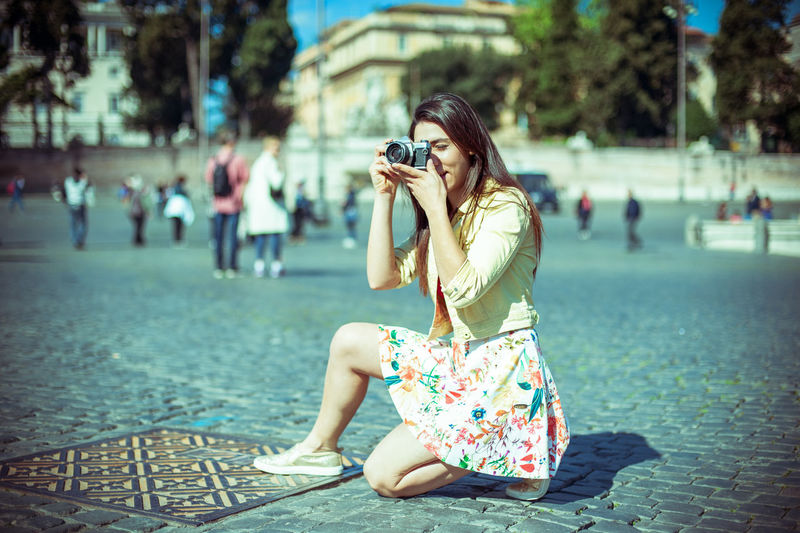 Full length of beautiful woman photographing by historic building against sky